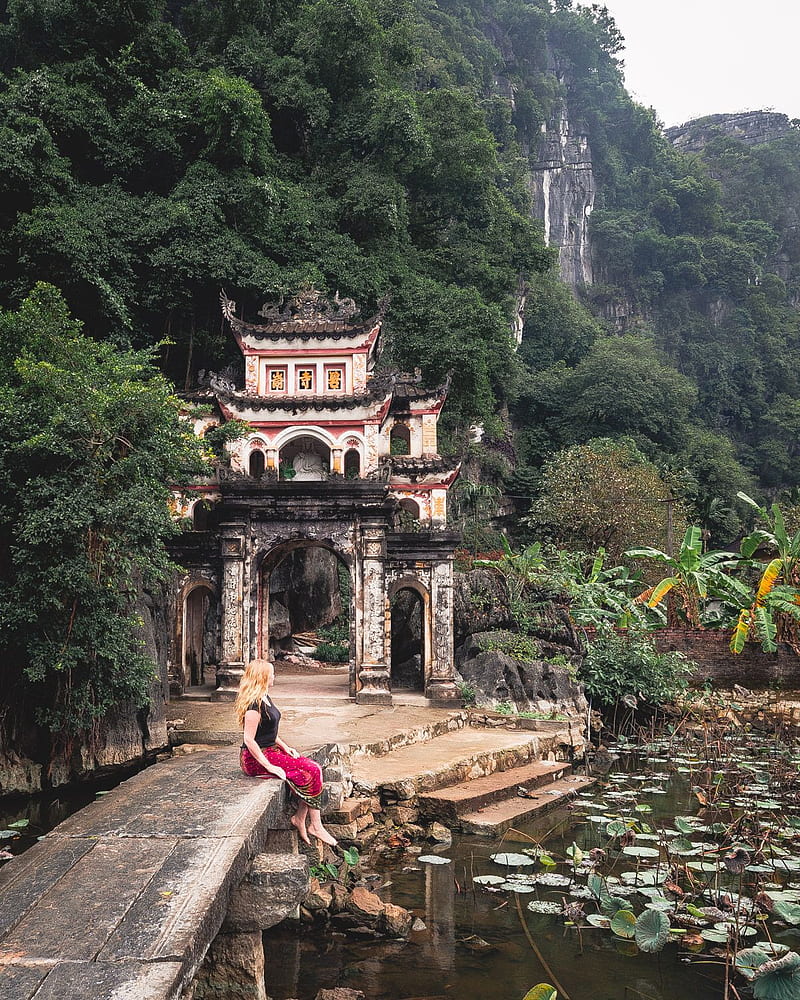 Premium Photo  Lone tourist with traditional vietnamese hat at bich dong  pagoda entrance gate, ninh binh vietnam, buddhist temple set amid jungle  and karst mountain range. traveling alone, keep social distancing.